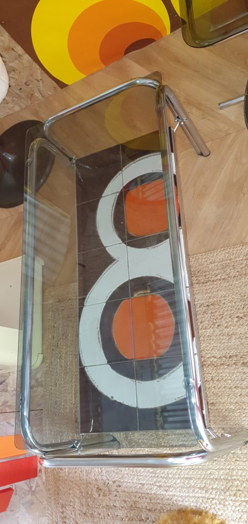 Table des années 70 pieds chromés, plateau supérieur en verre fumé et plateau inférieur en céramique avec formes géométriques typiques marron et orange