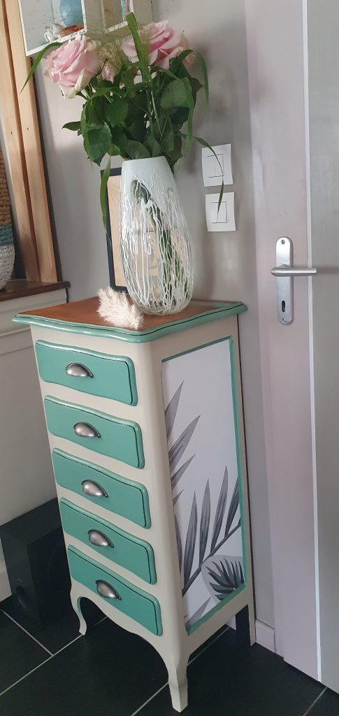 Chiffonnier entièrement refait et repeint dans des couleurs douces: lin et vert d'eau. Côtés retapissés ainsi que les tiroirs dans des motifs grandes feuilles grises.