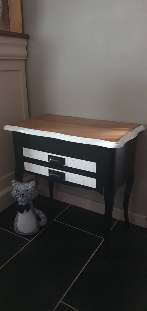 Meuble bas 2 tiroirs et plateau qui s'ouvre. Entièrement refait et peint en blanc et noir. Façades des tiroirs retapissés avec un papier peint blanc imitation croco. Pochoir pissenlit sur le côté gauche pour un touche de fantaisie et poésie.